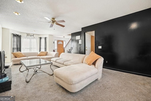 carpeted living area with a textured ceiling, ceiling fan, and stairs