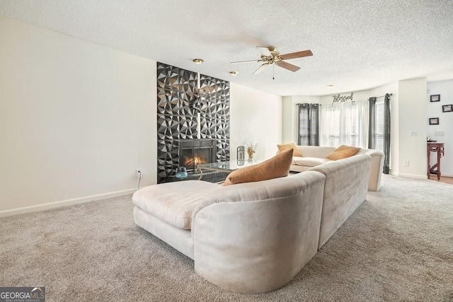 carpeted living area with baseboards, a fireplace, ceiling fan, and a textured ceiling