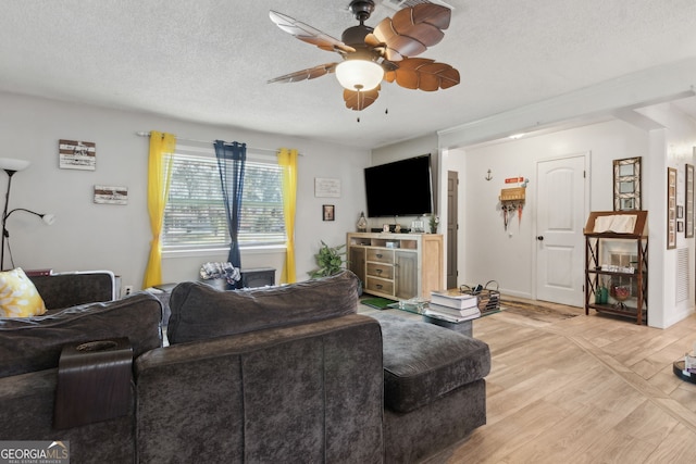 living area with baseboards, a ceiling fan, light wood-type flooring, and a textured ceiling