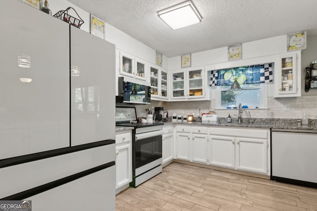 kitchen with dishwashing machine, freestanding refrigerator, a sink, electric stove, and white cabinetry