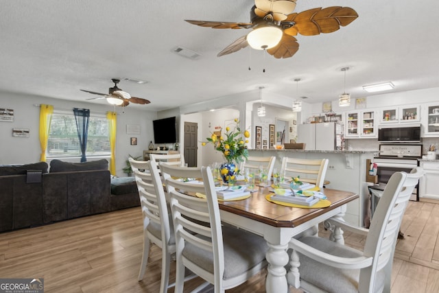 dining area with visible vents, a textured ceiling, light wood-type flooring, and a ceiling fan