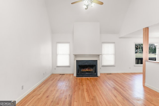 unfurnished living room with lofted ceiling, a warm lit fireplace, light wood-style floors, and a ceiling fan