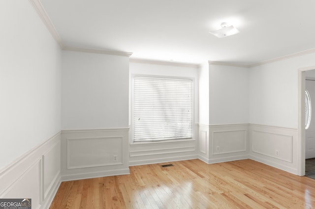 empty room featuring light wood-style flooring, visible vents, and ornamental molding