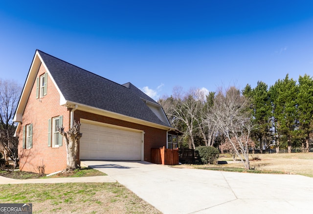 view of side of home featuring brick siding, a garage, concrete driveway, and roof with shingles