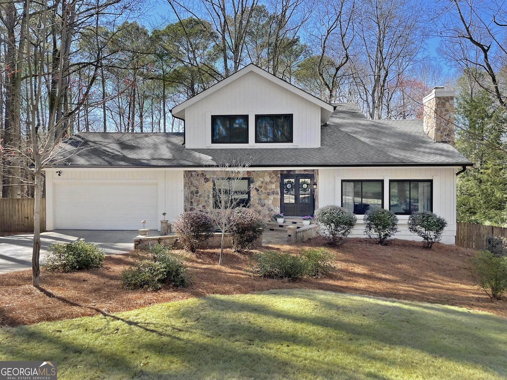 view of front facade with a front yard, a chimney, concrete driveway, french doors, and a garage