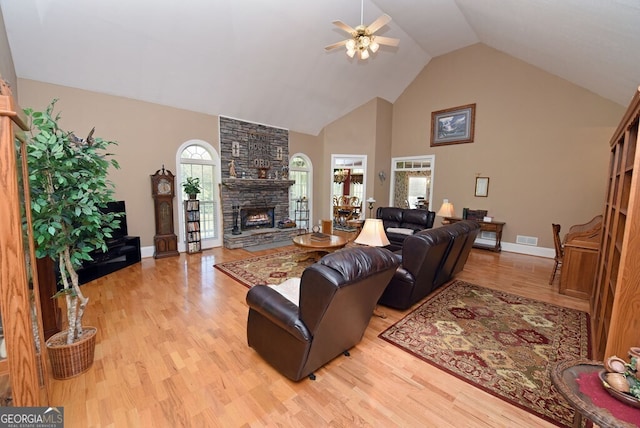 living room featuring visible vents, high vaulted ceiling, light wood-style flooring, a ceiling fan, and a stone fireplace