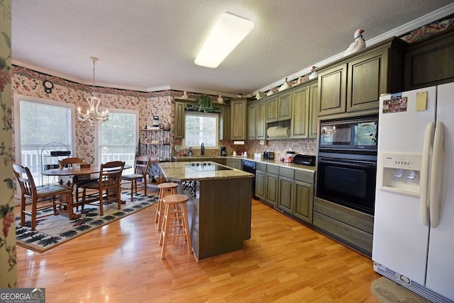 kitchen with a kitchen island, black appliances, light wood-style floors, green cabinets, and a chandelier