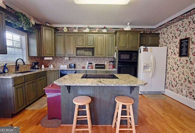 kitchen featuring wallpapered walls, a sink, black appliances, light wood-style floors, and a kitchen breakfast bar