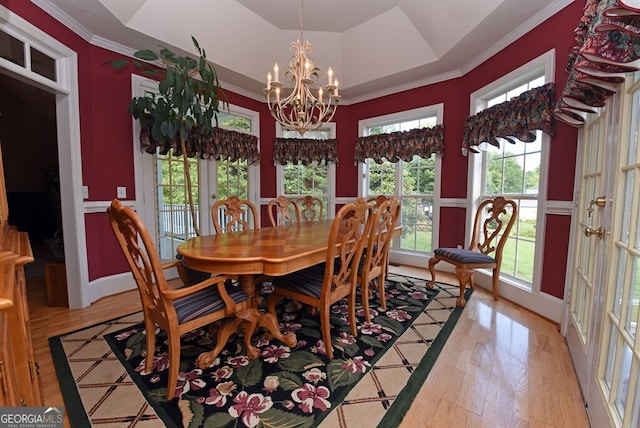 dining space featuring baseboards, an inviting chandelier, a tray ceiling, light wood-style flooring, and crown molding