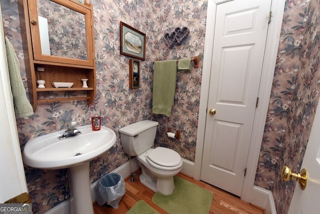 half bath featuring toilet, wallpapered walls, baseboards, and wood finished floors