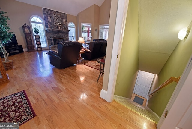 interior space featuring a fireplace, high vaulted ceiling, baseboards, and wood finished floors