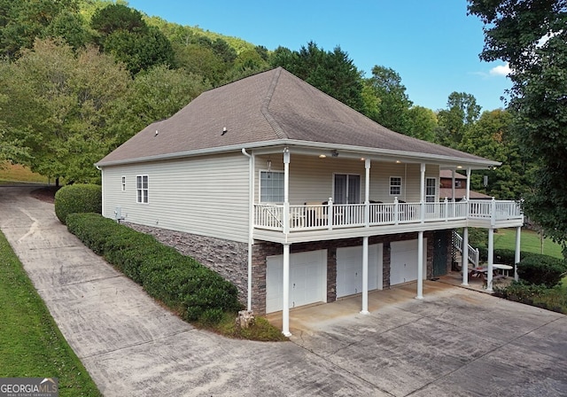 back of house featuring driveway, stone siding, covered porch, an attached garage, and stairs