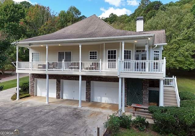 rear view of property with a porch, concrete driveway, stairs, roof with shingles, and a chimney