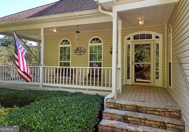 doorway to property featuring covered porch and a shingled roof