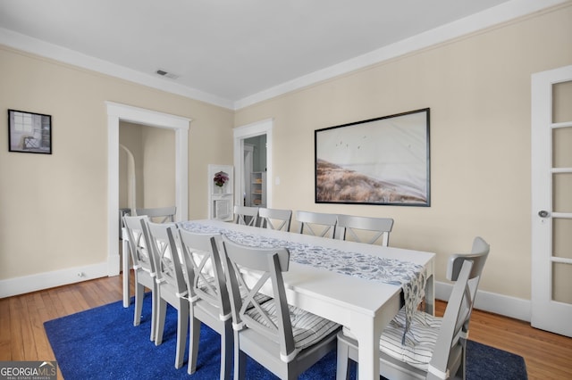 dining room featuring visible vents, crown molding, baseboards, and wood-type flooring