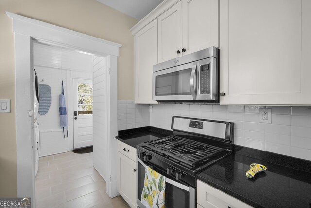 kitchen featuring dark stone countertops, tasteful backsplash, white cabinetry, stainless steel appliances, and light tile patterned floors