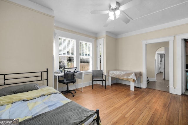 bedroom featuring baseboards, wood-type flooring, arched walkways, and ceiling fan