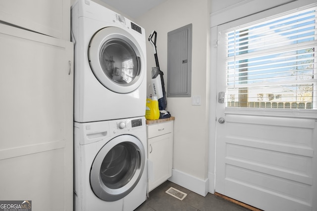 clothes washing area featuring visible vents, stacked washing maching and dryer, electric panel, cabinet space, and dark tile patterned floors