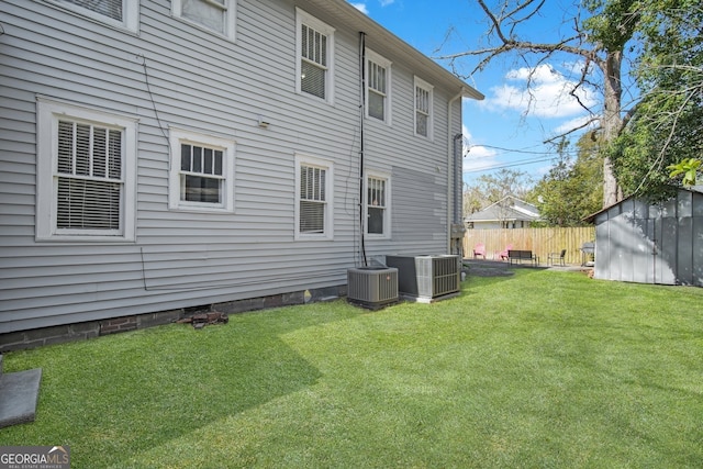 back of property featuring fence, a lawn, cooling unit, a storage shed, and an outbuilding