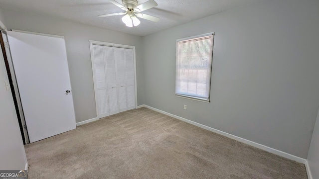 unfurnished bedroom with baseboards, ceiling fan, light colored carpet, a closet, and a textured ceiling