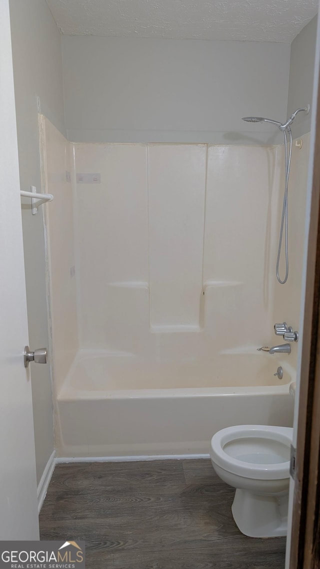 bathroom featuring toilet, wood finished floors, shower / bathtub combination, and a textured ceiling