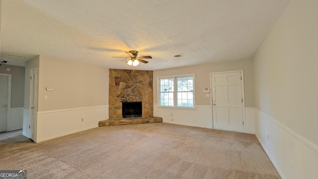 unfurnished living room featuring carpet, attic access, ceiling fan, a stone fireplace, and a textured ceiling