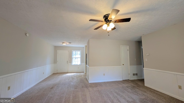 unfurnished room with visible vents, light carpet, a textured ceiling, wainscoting, and ceiling fan