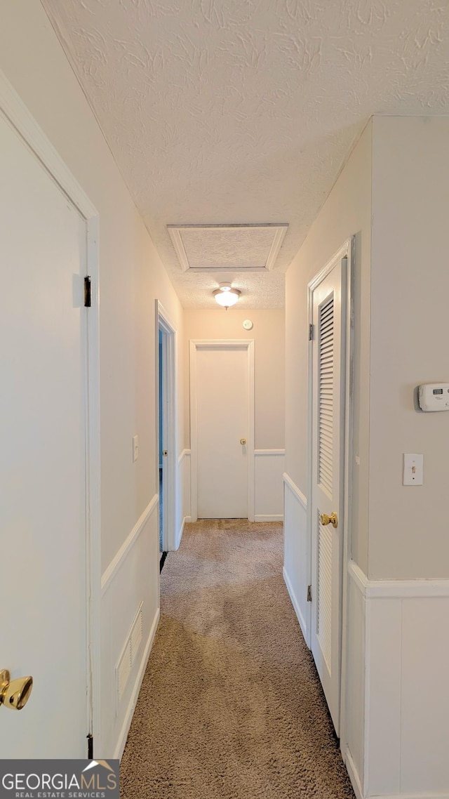 corridor with light carpet, visible vents, and a textured ceiling