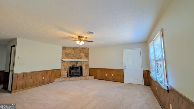 unfurnished living room with a wainscoted wall, visible vents, a ceiling fan, a textured ceiling, and carpet floors