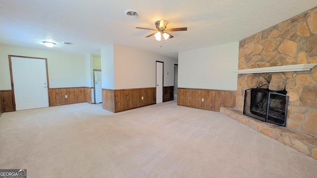 unfurnished living room featuring a wainscoted wall, visible vents, a ceiling fan, a textured ceiling, and a stone fireplace