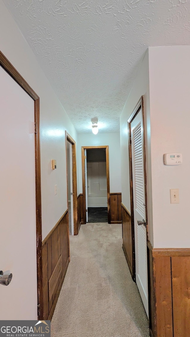 hallway featuring light carpet, a textured ceiling, wood walls, and wainscoting