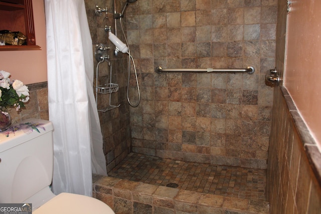 full bath with a wainscoted wall, a shower stall, toilet, and tile walls