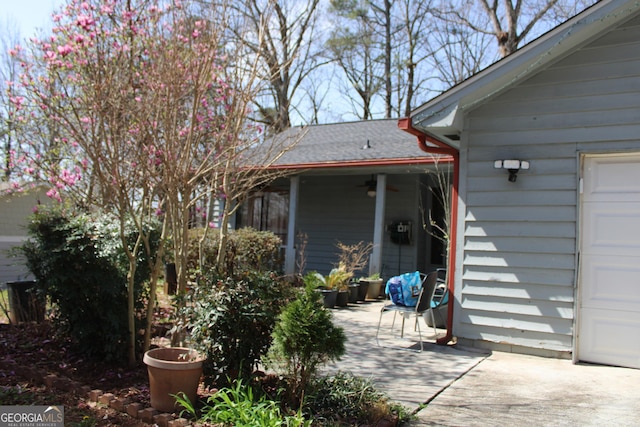 rear view of property featuring a garage, a shingled roof, and a ceiling fan