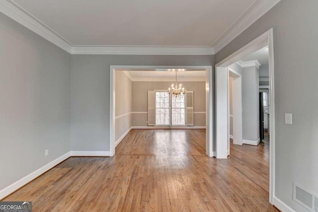 unfurnished room featuring visible vents, wood finished floors, an inviting chandelier, crown molding, and baseboards