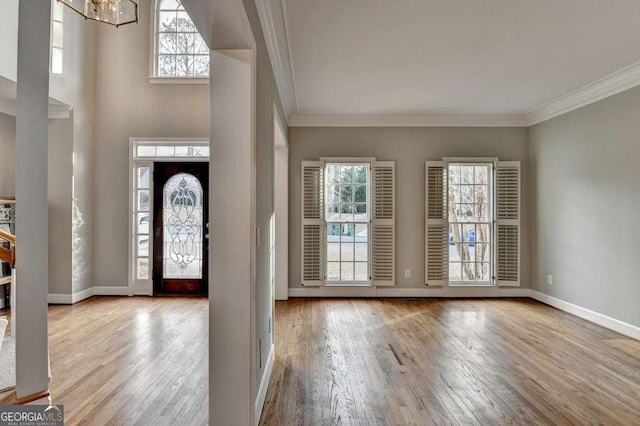 foyer entrance with crown molding, baseboards, wood finished floors, a towering ceiling, and an inviting chandelier