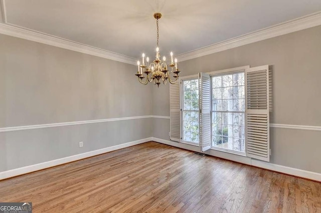 unfurnished room featuring wood finished floors, visible vents, baseboards, ornamental molding, and a chandelier