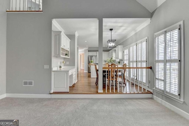 carpeted dining area featuring visible vents, baseboards, crown molding, and an inviting chandelier