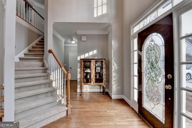 entryway with light wood-style flooring, baseboards, stairs, and a towering ceiling