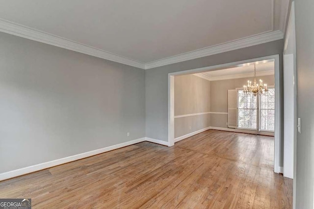 spare room with an inviting chandelier, crown molding, wood finished floors, and baseboards