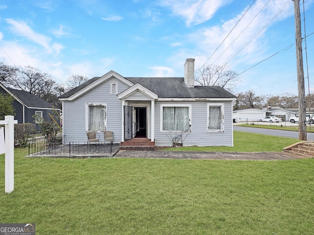 bungalow-style home with a chimney, a front lawn, and fence