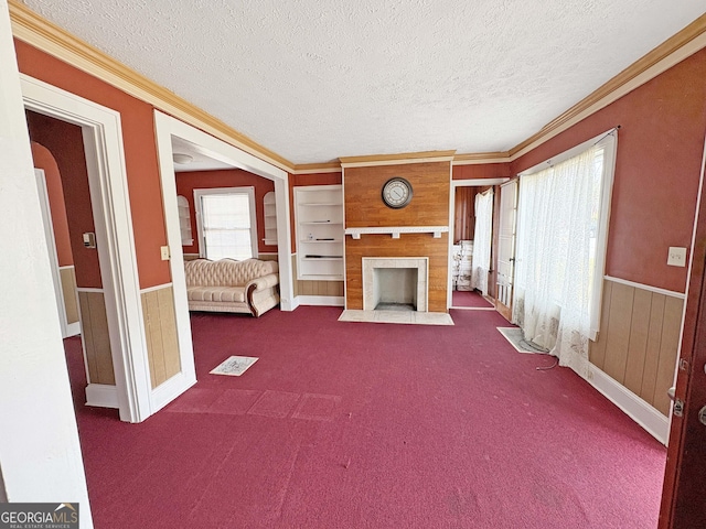 unfurnished living room with a wainscoted wall, a textured ceiling, crown molding, and dark colored carpet