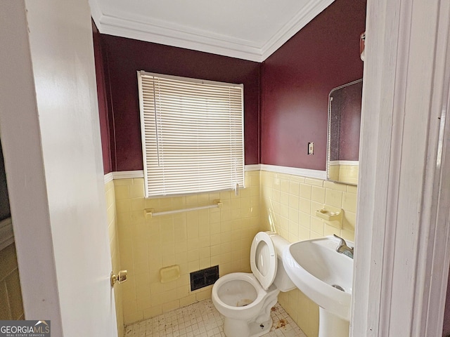 half bathroom with visible vents, a wainscoted wall, toilet, ornamental molding, and a sink