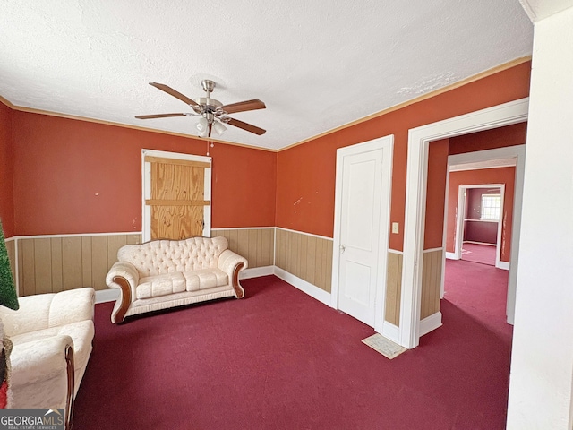 carpeted living area featuring wainscoting, a textured ceiling, and a ceiling fan