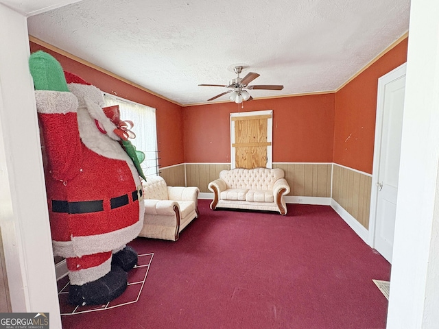 sitting room with ceiling fan, a wainscoted wall, wood walls, carpet flooring, and a textured ceiling