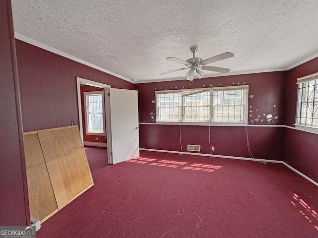 carpeted empty room with visible vents, a textured ceiling, ceiling fan, and crown molding