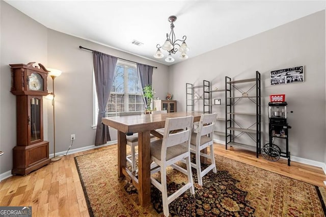 dining area featuring baseboards, a chandelier, visible vents, and light wood-style flooring