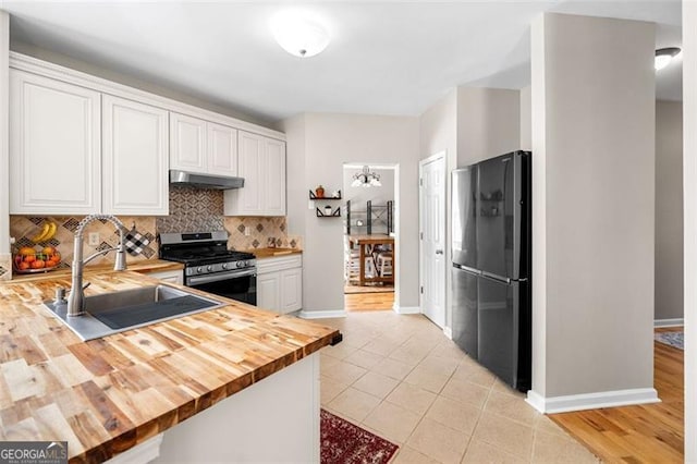 kitchen featuring stainless steel range with gas stovetop, a sink, freestanding refrigerator, butcher block countertops, and under cabinet range hood