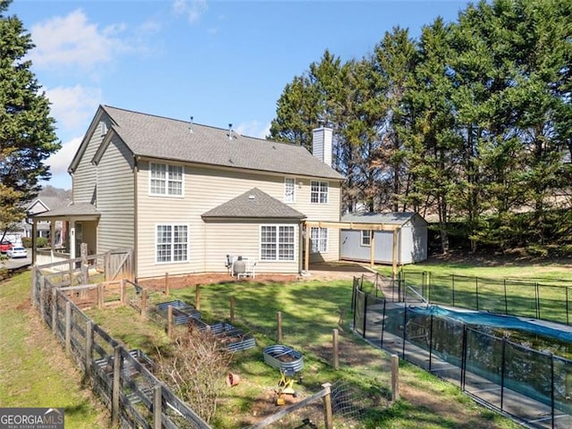 rear view of property featuring a chimney, a fenced backyard, an outbuilding, a lawn, and a storage unit