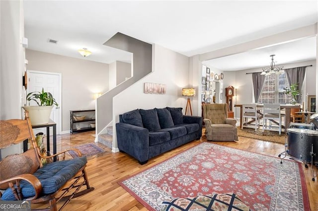 living room with wood finished floors, visible vents, an inviting chandelier, and stairs
