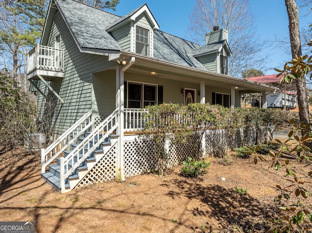 view of front of house featuring roof with shingles, covered porch, and a chimney